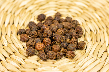 Lot of whole spicy black pepper on bamboo coaster