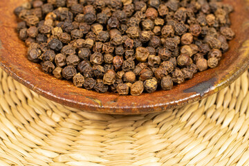Lot of whole spicy black pepper in ceramic bowl on bamboo coaster