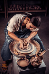 Beautiful artisan girl making pottery, sculptor from wet clay on wheel. Concept for woman in freelance, business, hobby.
