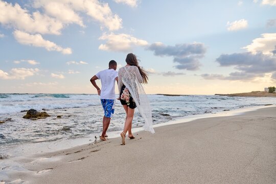 Happy couple running together on beach on summer day, back view