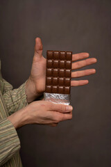 White man presenting chocolate bar in striped shirt on grey background