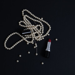 Red lipstick and white pearl necklace isolated on black background. Flat lay.