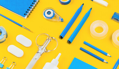 Assorted office and school white and blue stationery on bright yellow background. Organized...