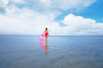 Enjoying suntan and vacation. Young woman in red swimsuit with pink rubber ring on the beach.