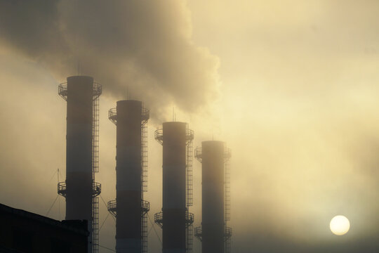 Four smoking chimneys against the background of the sun barely shining through the smog and fog.