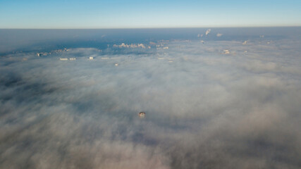 Obraz premium Silhouettes of tall houses through the incoming thick fog. Megalopolis in white clouds in the early morning at time.
