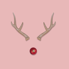 Abstract Christmas reindeer face made with antlers and a bauble decoration nose on a pastel pink background. © Jovica Varga
