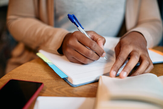 Close-up of black female student writes in notebook while learning in library.