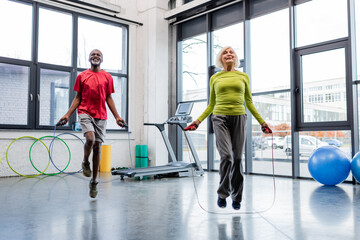 Smiling interracial people training with jump ropes in gym.