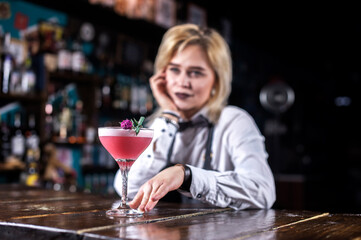 Young girl barman demonstrates his professional skills while standing near the bar counter in bar