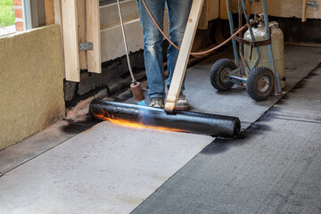 Installation of waterproofing on the concrete foundation by heating and melting rolls of bitumen...