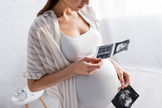 partial view of pregnant woman holding ultrasound photos.