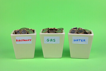 Three pots labelled electricity, gas and water filled with pound coins. Saving to pay utility bills.