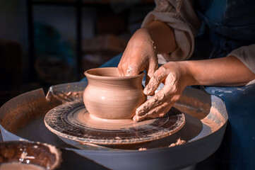 Close-up A woman potter in beautifully sculpts a deep bowl of brown clay and cuts off excess clay on a potter's wheel in a beautiful workshop