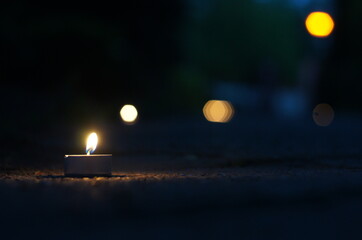 Mała świeczka leżąca na ziemi przed rozmytym tłem rozświetlająca ciemność.