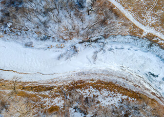 Close up overhead photo of frozen river covered in snow surrounded by winter scenery and frozen land in rural North Dakota. Brown, white and gold. Cold, desolate. 