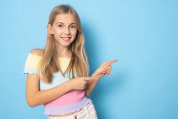 Little smiling girl in summer clothing pointing fingers side standing isolated over blue background.