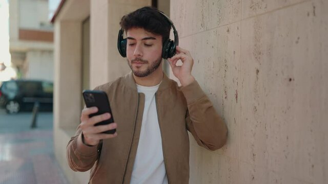 Young hispanic man smiling confident listening to music using smartphone at street