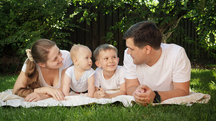 Happy smiling family with children lying on grass in garden and having fun. Parenting, family, children development, and fun outdoors in nature.