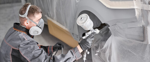 Painting the rear part of the car. Car painter wearing costume and protective gear. Car service...