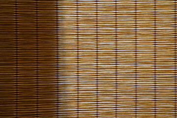 Light from the window comes through a curtain made of bamboo straw. Part of the surface is in shadow. Background. Texture.