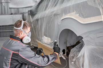 Painting the rear part of the car. Car painter wearing costume and protective gear. Car service...
