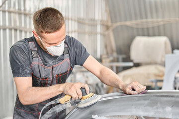 The mechanic works with a grinding tool. Sanding of car elements. Painting car service. Repairing car section after the accident.