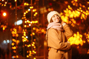 Young woman walks through the night winter city. Light around.  Winter fashion, holidays, rest, travel concept.