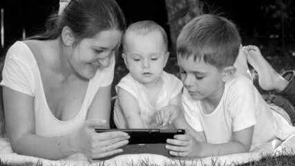 Black and white portrait of happy family with children relaxing in park and watching video on tablet computer