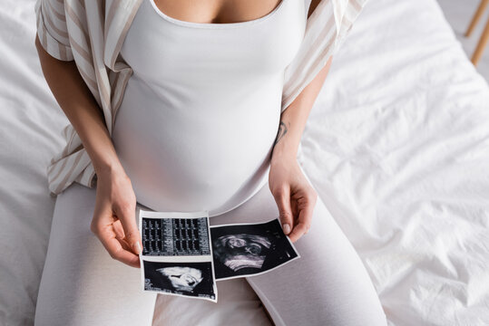 partial view of pregnant woman holding ultrasound pictures.