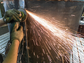 caucasian hands using an angle grinder on metal barrel vessel close-up with long sparks trails