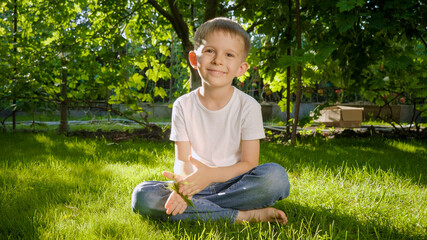 Dolly shot of 6 years old boy sitting on grass and looking in camera. Parenting, family, children development, and fun outdoors in nature. © Kyrylo Ryzhov