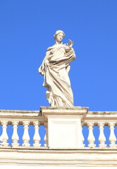 Fototapeta na wymiar St Peter's Basilica Colonnade Detail with White Statue of a Woman Saint Against a Bright Blue Sky in Rome, Italy