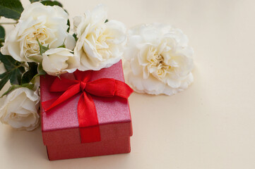 Fototapeta na wymiar gift red box and white roses on a beige background with a place for text
