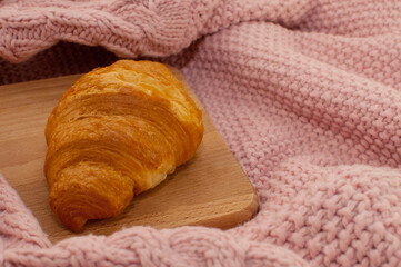 croissant on a wooden board on a pink knitted blanket