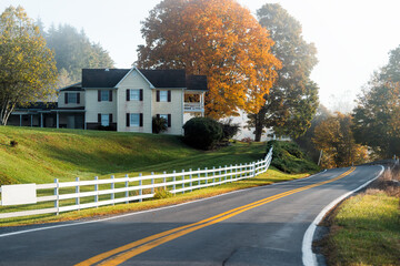 Roadside farmhouse house in countryside rural road highway in West Virginia, USA by mountain forest with colorful autumn fall trees foliage at sunrise morning - Powered by Adobe