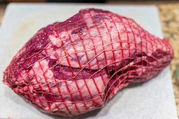 Red raw New Zealand or Australian lamb meat whole leg chunk with mesh packaging on cutting board...