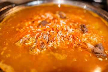 Lamb meat cooking with carrots on frying pan with rice as traditional Kazakh or Uzbek pilaf or plov macro closeup with orange color