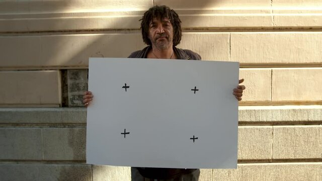 Homeless man holding a white placard outdoors