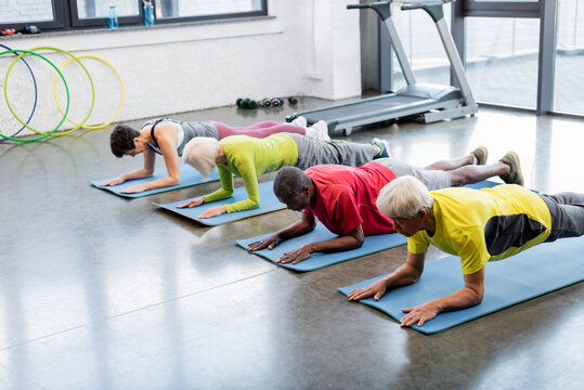 Elderly multiethnic people standing in plank on fitness mats.