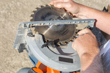 a man replaces the saw blade of an electric miter saw for woodworking. Repair and maintenance of...