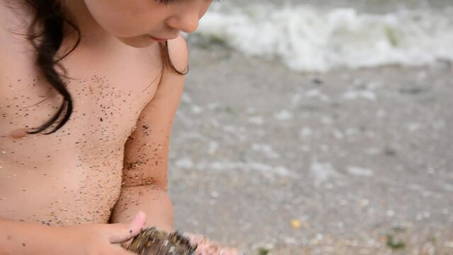 Little girl is playing on the beach. Happy child at the sea. Children's hands in the sea sand. Summer. The child plays on the seashore. The child builds a sand castle. Children's concept. 