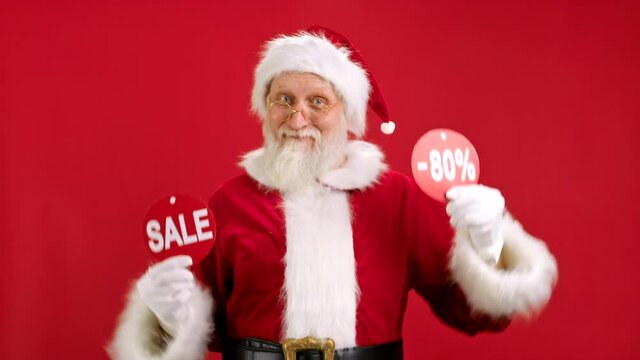 Christmas SALE -80 Off. Cheerful Santa Claus is Dancing and Joyful From Christmas Sale Holding Two Banners With Inscription SALE and -80 Off Showing Off Inscriptions to Camera on Red Background.