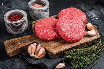 Raw veal hamburger patties with herbs and spices. Black background. Top view