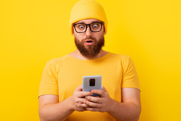 shocked man looking at phone over yellow background