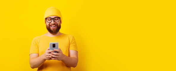 smiling man looking at phone over yellow background, panoramic layout