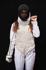 Portrait of a young fencer wearing white fencing costume and mask and holding the sword in front of...