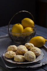 Round lemon cookies on a white plate surrounded by lemons fruit, gray wooden background. Homemade cookies