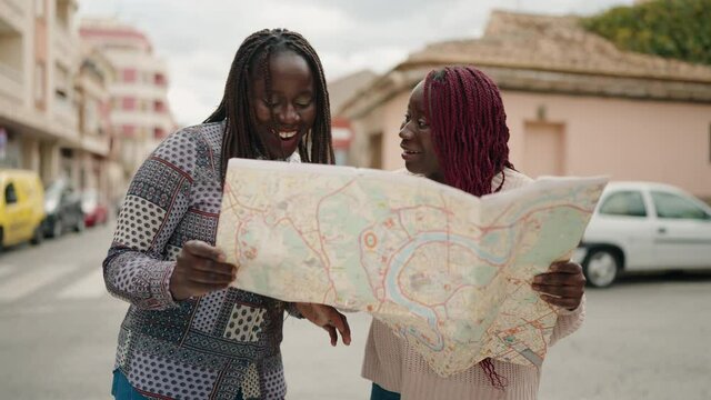 Two african american women smiling confident looking map at street