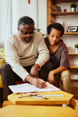 Obraz premium An African grandfather showing to his grandson how to solve a math problem. Family support